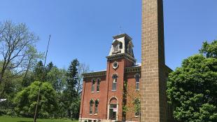 A brick custom-built Chimney Swift Tower stands in front of a historic schoolhouse that is now the home of public radio station WYSO in Yellow Springs, Ohio.