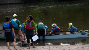 Lillian Holden stands on a dock guiding people boarding a canoe