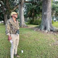 Professor Drew Lanham stands beneath large trees on bank of a former rice plantation in Virginia.