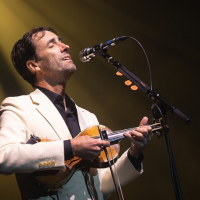 Man stands singing at microphone, strumming a violin