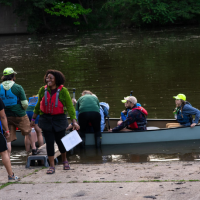 Lillian Holden stands on a dock guiding people boarding a canoe