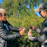 Two women face each other, each holding a small bird in their hands. Lisa Kizuik is on the left of the image.